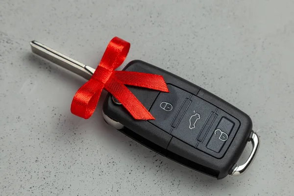 灰色の背景に弓と赤いリボンで結ばれた贈り物として車のキー. — ストック写真