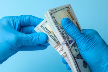 Doktor mavi eldiven mavi arka plan üzerinde nakit dolar para tutar. Rüşvet, yolsuzluk veya maaş kavramı.