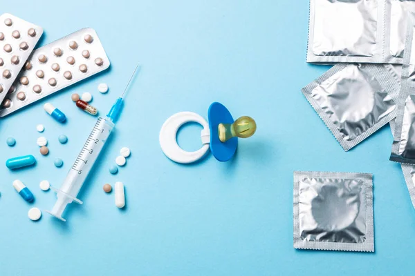 Birth control pills, an injection syringe and condom in a package on blue background. The concept of choosing method of contraception, birth control pills or condom. Baby nipple as symbol of pregnancy