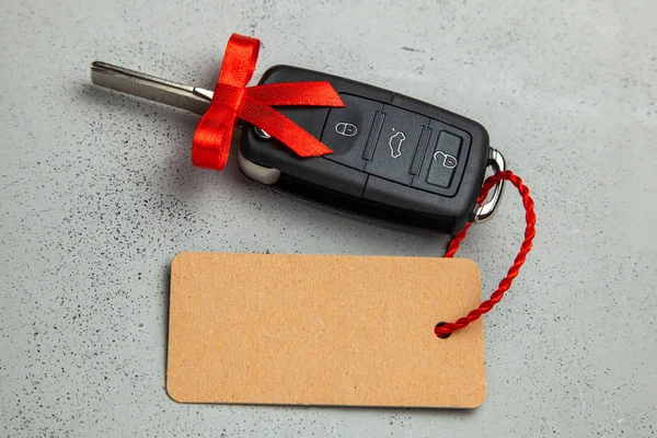 弓とラベルのタグに赤リボン付きリモコン アラーム付きの車の鍵をプレゼントします。灰色の背景. — ストック写真
