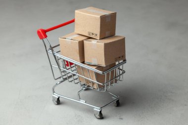 Online mağaza mal satın alma. Gri arka plan üzerinde alışveriş sepetindeki karton kutular.