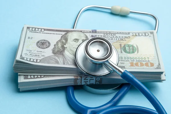Pila di dollari in contanti e stetoscopio su sfondo blu. Il concetto di strechevka medico o medicina costosa Foto Stock Royalty Free