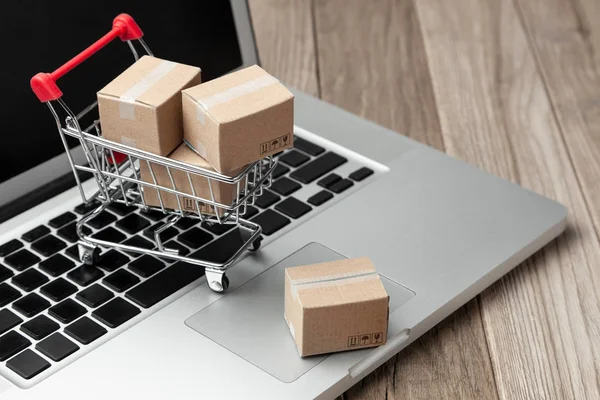 Levering van de bestelling uit de online winkel. Online winkelen. Dozen met goederen in het winkelmandje op de tafel met laptop — Stockfoto