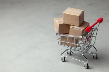 Online mağaza mal satın alma. Gri arka plan üzerinde alışveriş sepetindeki karton kutular.