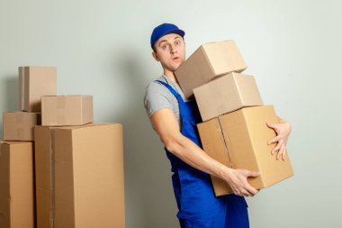 Hareketli bir gün. Online mağazada alışveriş teslim mal. Yükleyici veya kurye gri duvara karton kutular taşıma