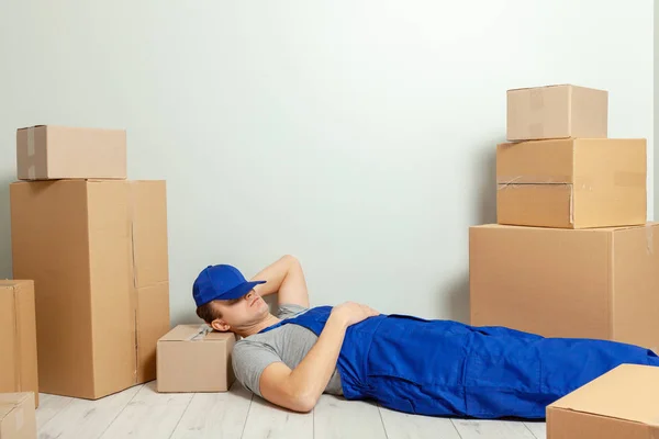 Day moving. Delivery of goods from shopping in the online store. The loader or courier has break and sleeps in the workplace against the background of gray wall