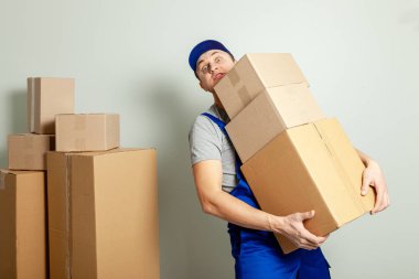 Hareketli bir gün. Online mağazada alışveriş teslim mal. Yükleyici veya kurye gri duvara karton kutular taşıma