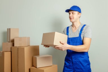 Hareketli bir gün. Online mağazada alışveriş teslim mal. Yükleyici veya kurye gri duvara karton kutular taşıma