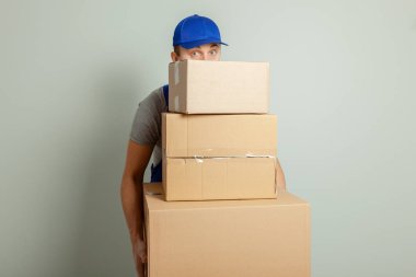 Hareketli bir gün. Online mağazada alışveriş teslim mal. Yükleyici veya kurye gri duvara karton kutular taşıma