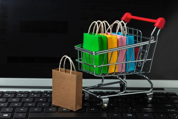 Membeli barang dan pakaian di toko online. Shopping bags in shopping cart on laptop keyboard — Stok Foto