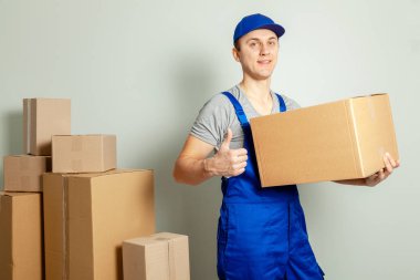 Hareketli bir gün. Online mağazada alışveriş teslim mal. Yükleyici veya kurye gri duvara karton kutular taşıma