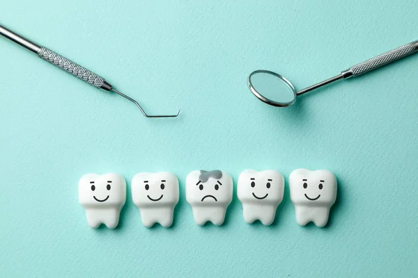 Healthy white teeth are smiling and  tooth with caries is sad on green mint background and dentist tools mirror, hook.