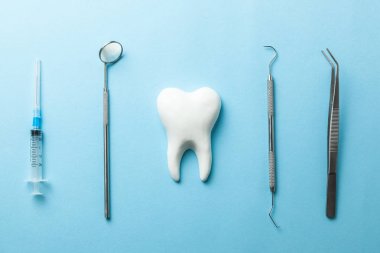 Mavi arka planda diş ve diş aletleri. Diş tedavisi. Diş hekimi araçları ayna, kanca, cımbız, şırınga.