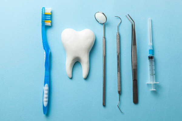 Tooth and dental instruments on blue background. Dental treatment. Dentist tools mirror, hook, tweezers, syringe and toothbrush