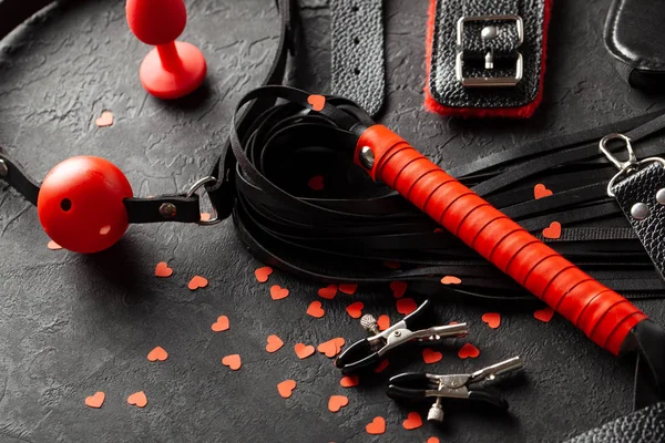 BDSM Sexleksaker för vuxna. Små röda hjärtan på svart bakgrund piska, gag, handbojor och läderremmar — Stockfoto