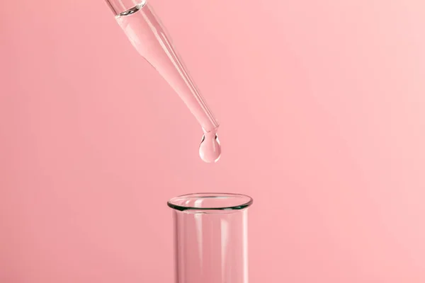 Drop the pipette into the test tube. The study of biological material. Laboratory research. Pink background.