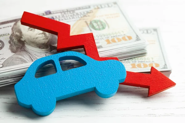 Röd pil grafik ner på bakgrunden av bilen och en bunt pengar kontanter dollar. Begreppet fallande bilmarknad, försäkring, lägre priser, reparationskostnader. — Stockfoto