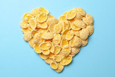 Yellow flakes in the shape of a heart on a blue background. I like breakfast cereal.