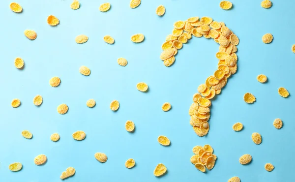 Copos amarillos en forma de signo de interrogación sobre un fondo azul. Cómo elegir el cereal para el desayuno o lo que hacen los cereales . — Foto de Stock