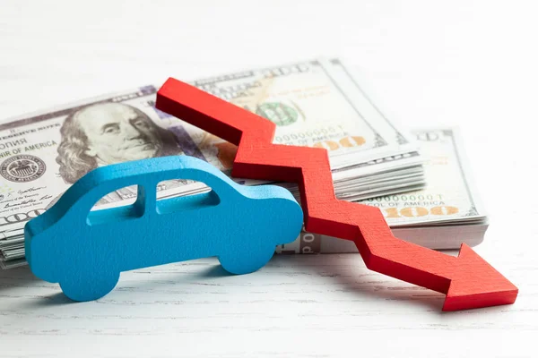 Röd pil grafik ner på bakgrunden av bilen och en bunt pengar kontanter dollar. Begreppet fallande bilmarknad, försäkring, lägre priser, reparationskostnader. — Stockfoto