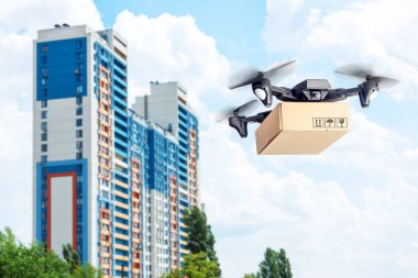Karton kutulu drone hava yoluyla teslimat yapar. Kameralı drone posta paketi taşıyor. Arka plan daire evi ve bulutlar gökyüzü