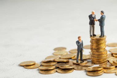 İşadamları, başarılı kârlı bir işlemin sembolü olarak el sıkışıyor. Başarı veya başarılı yatırımların sembolü olarak altın sikke yığını üzerinde Işadamları