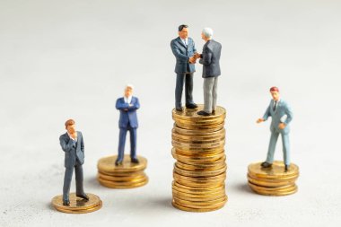 İşadamları, başarılı kârlı bir işlemin sembolü olarak el sıkışıyor. Başarı veya başarılı yatırımların sembolü olarak altın sikke yığını üzerinde Işadamları