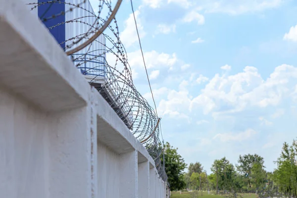 Betongvägg med taggtråd mot himlen med moln. — Stockfoto