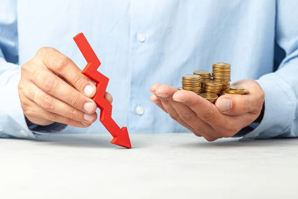 Man in blue shirt holds a down arrow and coins in his hand. Concept of falling profits or business bankruptcy. — Stock Photo, Image