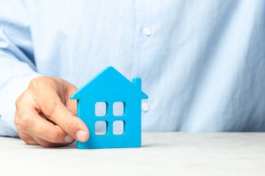 Mavi gömlekli adam elinde ev tutuyor. Concept emlakçı ev veya gayrimenkul kredisi satın almak için teklifler