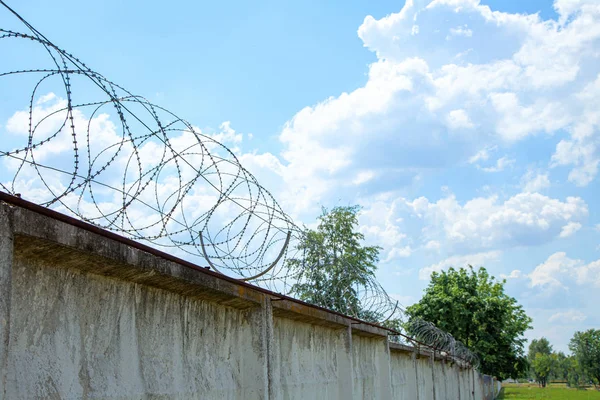 Betongvägg med taggtråd mot himlen med moln. — Stockfoto