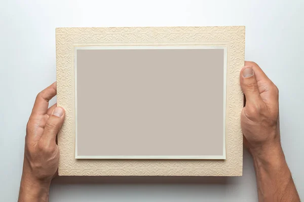 Old photo in frame in the hands of man. Empty template for picture, mock-up. Gray background.