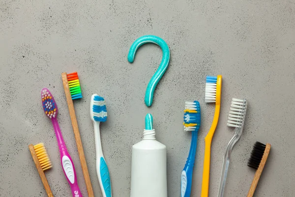 Dentifricio sotto forma di un punto interrogativo e molti spazzolini da denti diversi e colorati. Concetto di come scegliere lo spazzolino da denti giusto o come lavarsi i denti — Foto Stock