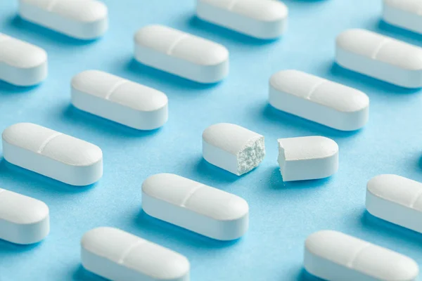 Bílé pilulky na modrém pozadí. Jedna tableta je rozbitá na polovinu, což snižuje dávku léku — Stock fotografie