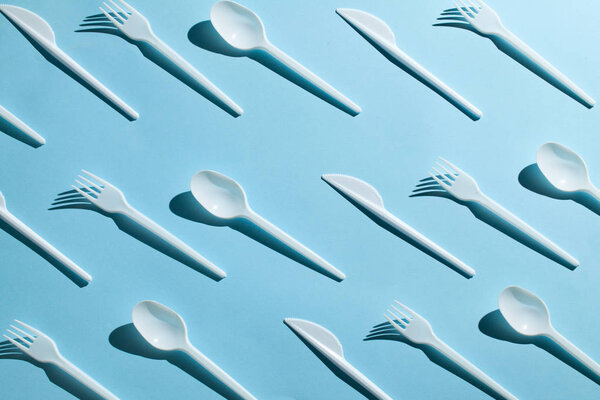 Plastic cutlery, forks, spoons and knives. Pollution of the environment with plastic and microplastics. Blue background