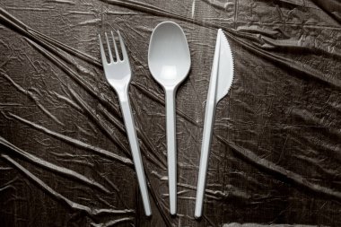 Plastik çatal, çatal, kaşık ve bıçaklar. Plastik ve mikroplastiklerle çevre kirliliği. Siyah plastik arkaplan