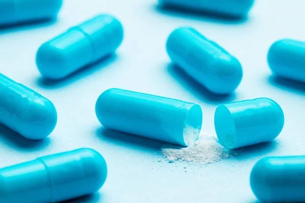 Blue tablets in capsules. One capsule is open. Blue background — Stock Photo, Image