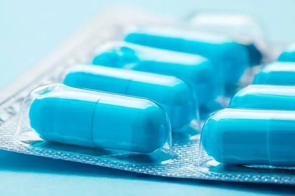 Comprimidos azules en cápsulas. Una cápsula está abierta. Fondo azul — Foto de Stock