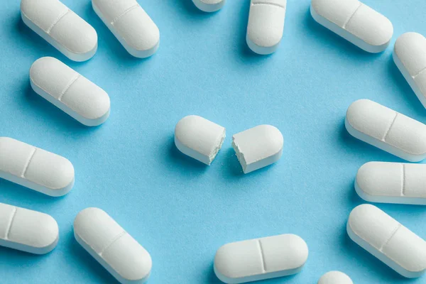 White pills on blue background. One tablet is broken in half, reducing the dose of the medicine — Stock Photo, Image