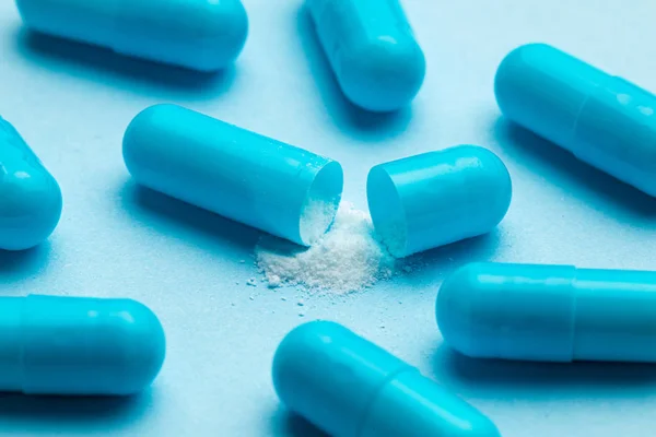 Blue tablets in capsules. One capsule is open. Blue background — Stock Photo, Image