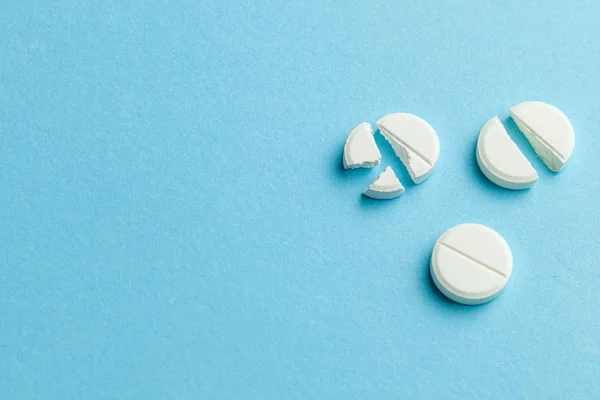 Белые таблетки на синем фоне. Несколько таблеток разбиты пополам, уменьшая дозу лекарства. Копирование текста . — стоковое фото