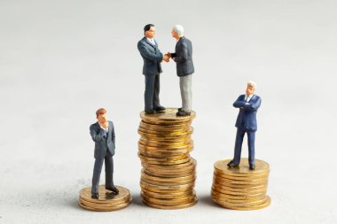 İşadamları, başarılı kârlı bir işlemin sembolü olarak el sıkışıyor. Başarı veya başarılı yatırımların sembolü olarak altın sikke yığını üzerinde Işadamları