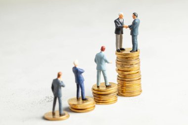 İşadamları başarılı bir alışverişin sembolü olarak el sıkışıyor. Başarı veya başarılı yatırımların sembolü olarak basamakları olan altın sikke yığınındaki işadamları