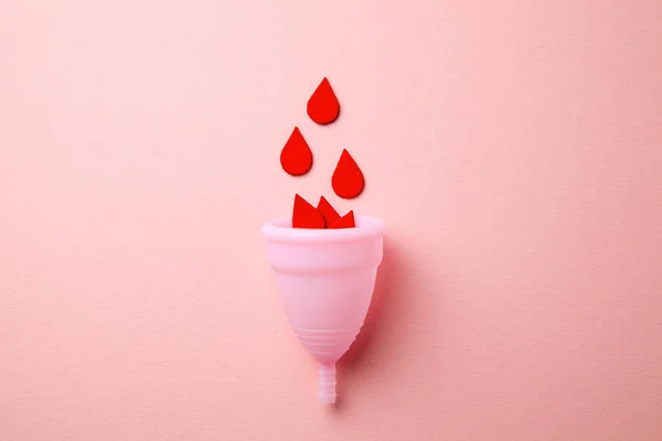 Copo menstrual de silicone. Saúde das mulheres e higiene alternativa. Copo com gotas de sangue em um fundo rosa . — Fotografia de Stock