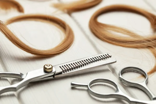 Cut hair curls and thinning scissors on a white wooden background