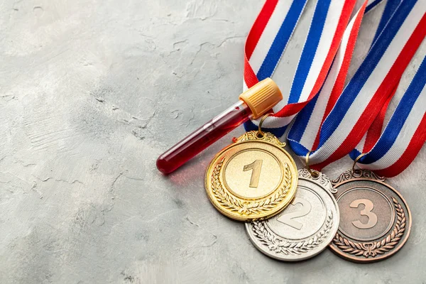 Prueba de dopaje. Medalla de oro, plata y bronce y tubo de ensayo con sangre sobre fondo gris — Foto de Stock