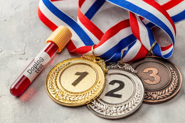 Prueba de dopaje. Medalla de oro, plata y bronce y tubo de ensayo con sangre sobre fondo gris — Foto de Stock