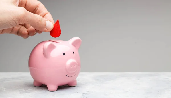 Blood donor. A man holds a red drop of blood in his hand and puts it in a piggy bank as a donation — Stock Photo, Image