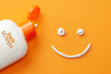 Sunscreen on orange background. Plastic bottle of sun protection and white cream in the shape of Smiley, smiling face clipart