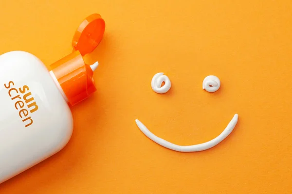 Солнцезащитный крем на оранжевом фоне. Пластиковая бутылка солнцезащиты и белый крем в форме смайлика, улыбающееся лицо — стоковое фото